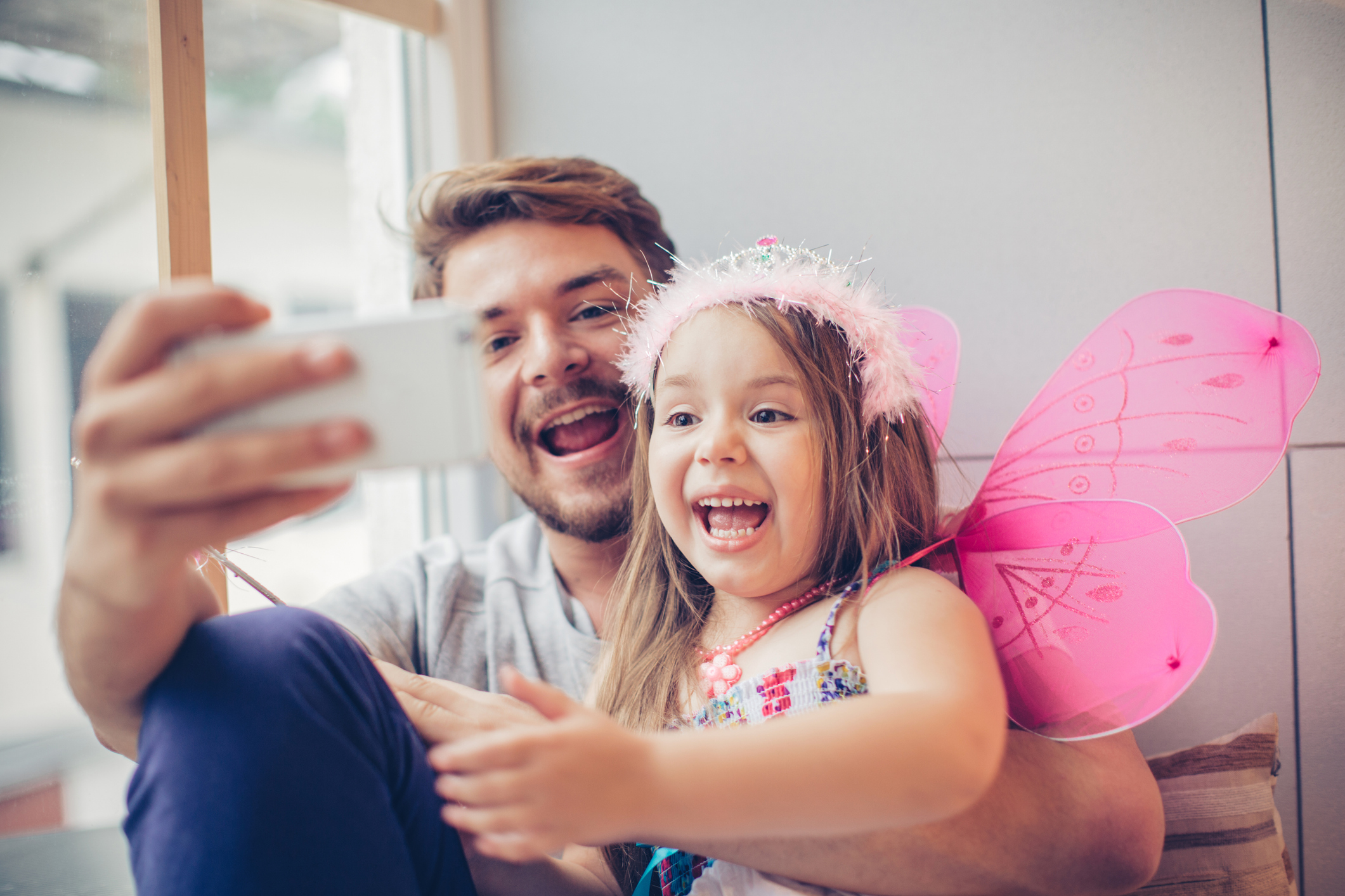 Un papà sorridente fa un selfie con una bambina che ride. Il tema dello sharenting e i rischi della condivisione di foto di minori online.